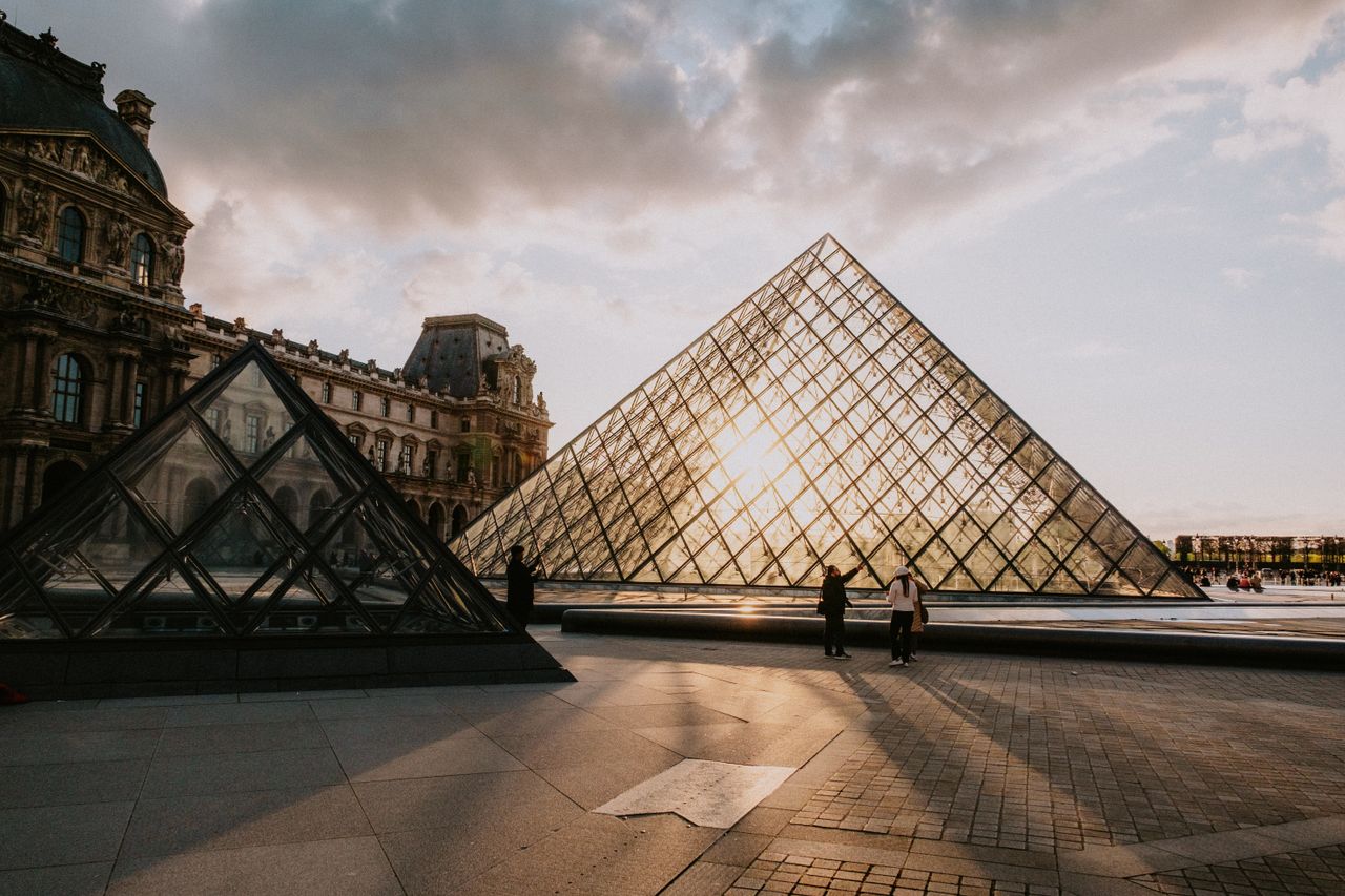 The iconic Louvre Pyramid glows with the sunset in the backdrop of Paris, France.